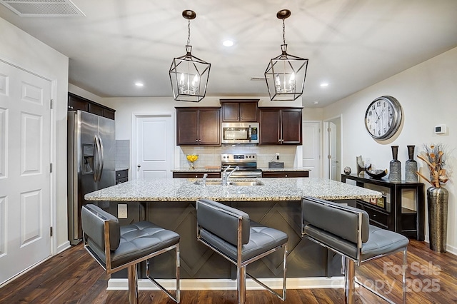 kitchen with a kitchen bar, visible vents, a sink, stainless steel appliances, and dark brown cabinets