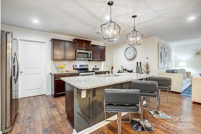 kitchen featuring a kitchen bar, a sink, backsplash, dark wood-style floors, and appliances with stainless steel finishes