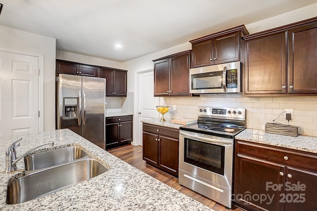 kitchen featuring a sink, stainless steel appliances, decorative backsplash, light stone countertops, and dark wood-style flooring