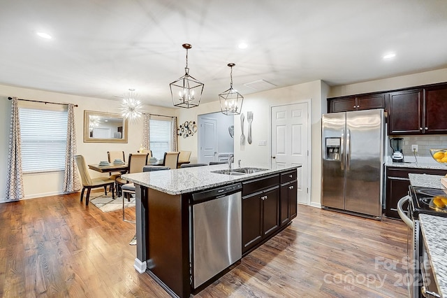 kitchen with wood finished floors, a center island with sink, dark brown cabinetry, appliances with stainless steel finishes, and tasteful backsplash