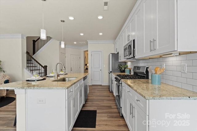 kitchen with dark wood finished floors, a sink, appliances with stainless steel finishes, white cabinetry, and a kitchen breakfast bar