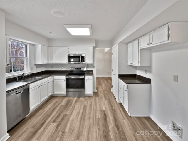 kitchen with light wood-type flooring, a sink, dark countertops, white cabinetry, and stainless steel appliances