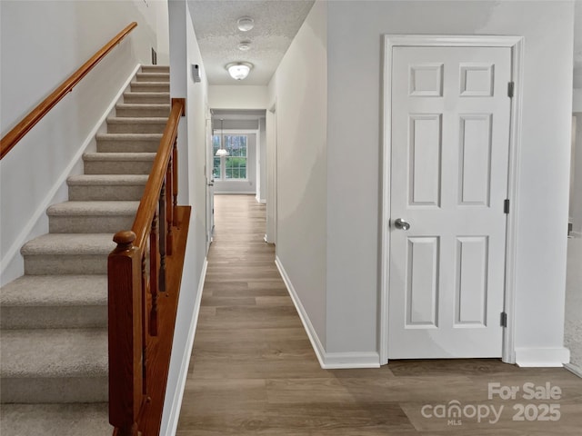 corridor featuring stairway, a textured ceiling, baseboards, and wood finished floors