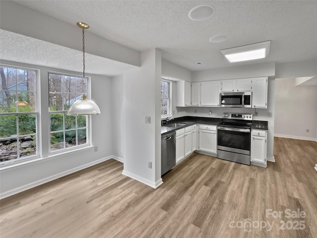 kitchen with light wood-style flooring, a sink, dark countertops, appliances with stainless steel finishes, and white cabinets