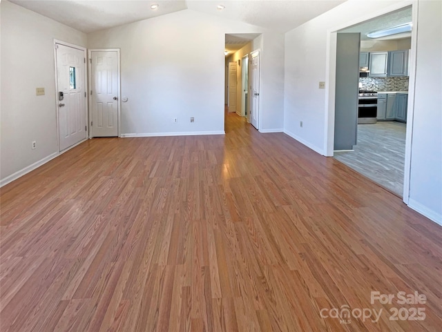 unfurnished living room with vaulted ceiling, baseboards, and light wood finished floors