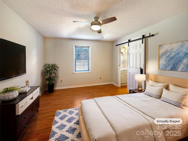 bedroom with ceiling fan, baseboards, a barn door, wood finished floors, and a textured ceiling