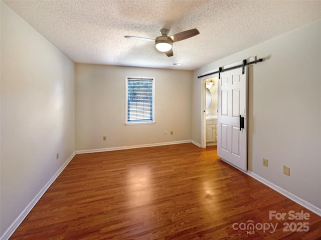 unfurnished bedroom featuring baseboards, a barn door, wood finished floors, a textured ceiling, and a ceiling fan