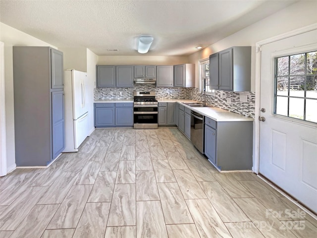 kitchen with gray cabinets, a sink, backsplash, stainless steel appliances, and light countertops