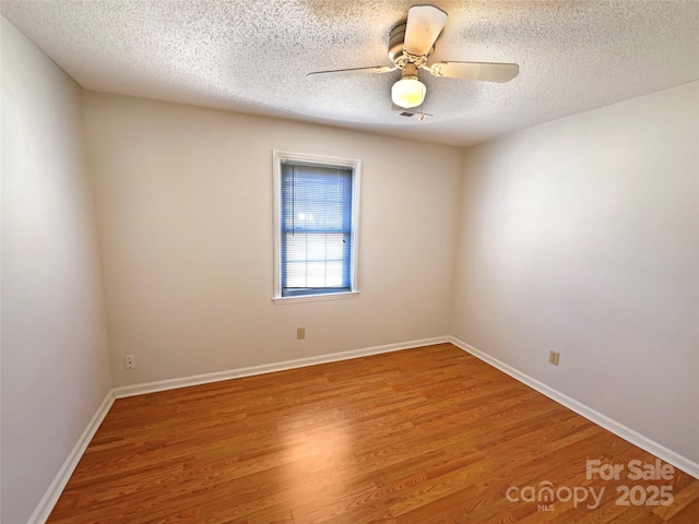 empty room with a ceiling fan, wood finished floors, baseboards, and a textured ceiling