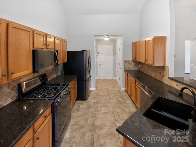 kitchen with dark stone countertops, high vaulted ceiling, appliances with stainless steel finishes, and a sink