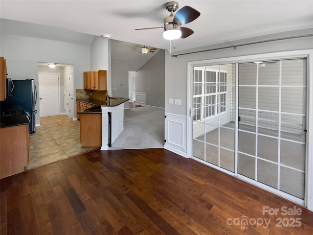 kitchen with dark countertops, a peninsula, wainscoting, lofted ceiling, and dark wood-style flooring