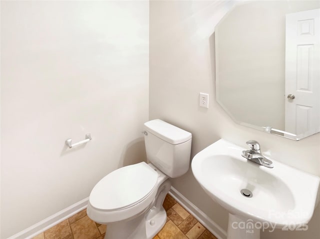 half bath featuring toilet, baseboards, and a sink