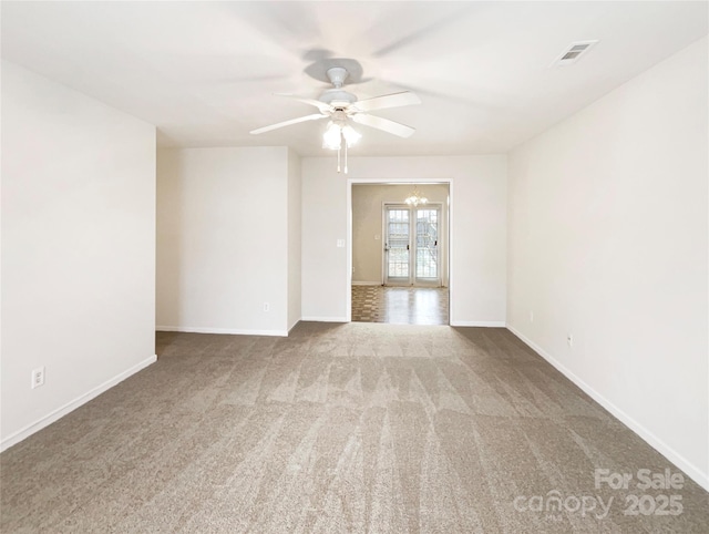 carpeted empty room featuring ceiling fan with notable chandelier, baseboards, and visible vents