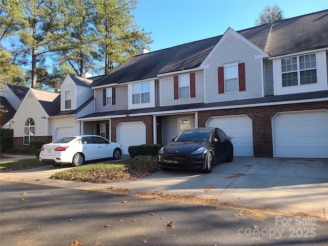 view of property with a garage, brick siding, a chimney, and driveway