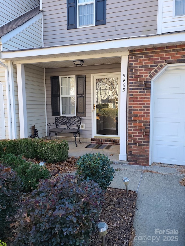 entrance to property featuring a porch, a garage, and brick siding