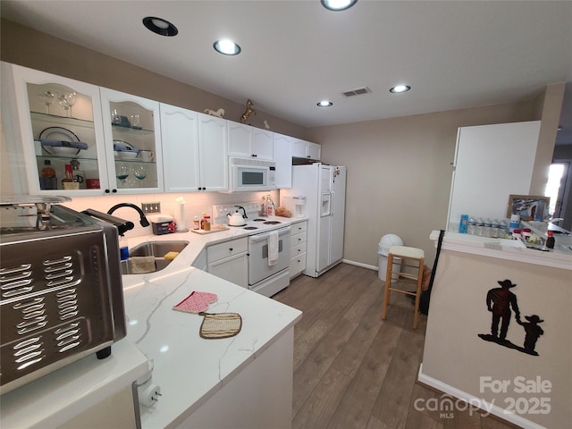 kitchen with white appliances, light stone counters, visible vents, a sink, and white cabinets