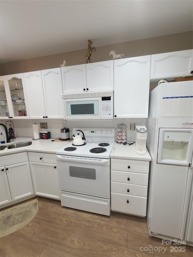 kitchen featuring light wood finished floors, glass insert cabinets, white appliances, white cabinetry, and a sink