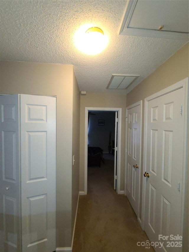 hallway featuring carpet, baseboards, and a textured ceiling