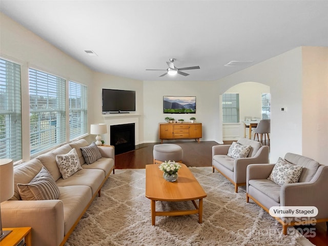 living room featuring light wood finished floors, visible vents, ceiling fan, a fireplace, and arched walkways