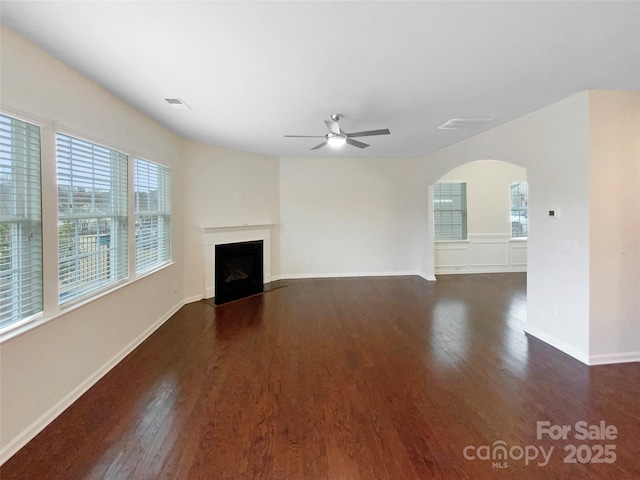 unfurnished living room with visible vents, a fireplace with flush hearth, a ceiling fan, arched walkways, and dark wood-style flooring