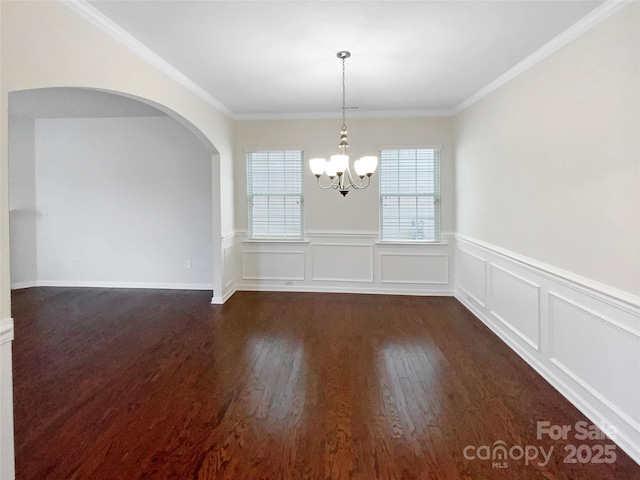 spare room featuring a chandelier, ornamental molding, arched walkways, and dark wood-style flooring