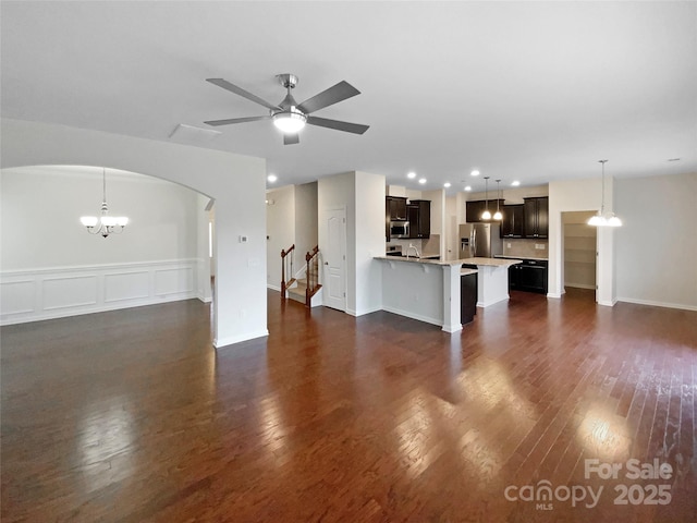 unfurnished living room with recessed lighting, arched walkways, dark wood-style flooring, and ceiling fan with notable chandelier