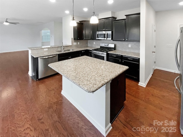 kitchen with a kitchen island, a peninsula, a sink, stainless steel appliances, and dark wood-type flooring