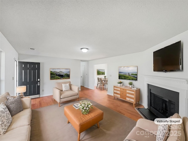 living room with visible vents, a fireplace with raised hearth, a textured ceiling, and wood finished floors