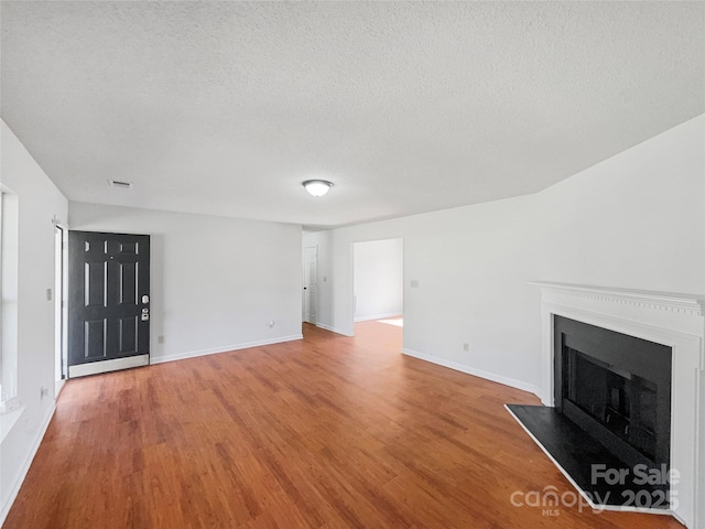 unfurnished living room featuring a fireplace with flush hearth, wood finished floors, baseboards, and a textured ceiling