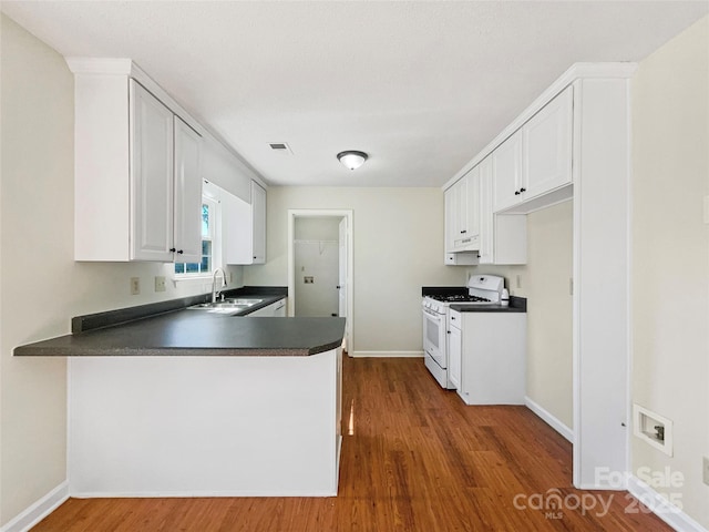 kitchen with white gas stove, a sink, dark countertops, a peninsula, and white cabinets