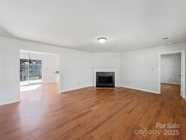 unfurnished living room with a chandelier, a fireplace with flush hearth, baseboards, and wood finished floors