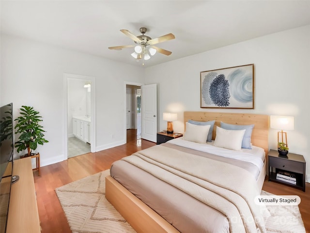 bedroom featuring baseboards, ensuite bath, wood finished floors, and a ceiling fan