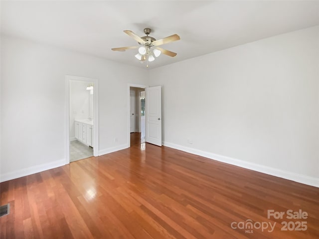 unfurnished bedroom with visible vents, a ceiling fan, ensuite bathroom, wood finished floors, and baseboards