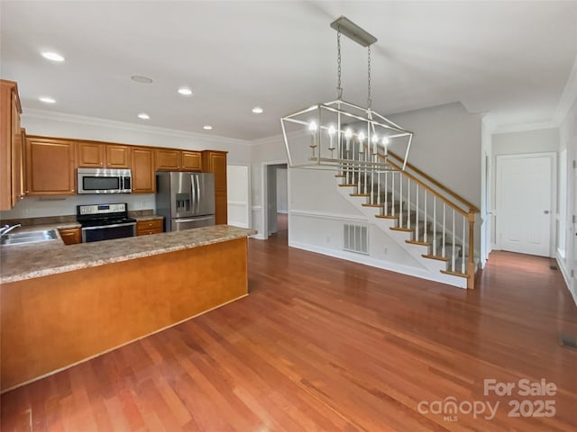 kitchen with a notable chandelier, brown cabinets, stainless steel appliances, and wood finished floors