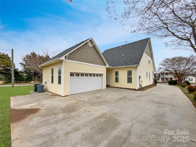 view of side of property with cooling unit, driveway, roof with shingles, an attached garage, and a yard