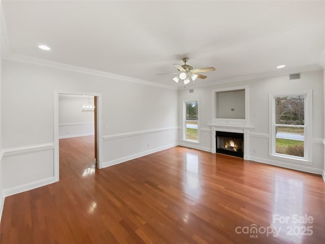 unfurnished living room with visible vents, a warm lit fireplace, wood finished floors, and crown molding