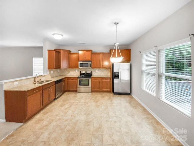 kitchen with backsplash, pendant lighting, brown cabinets, stainless steel appliances, and a sink