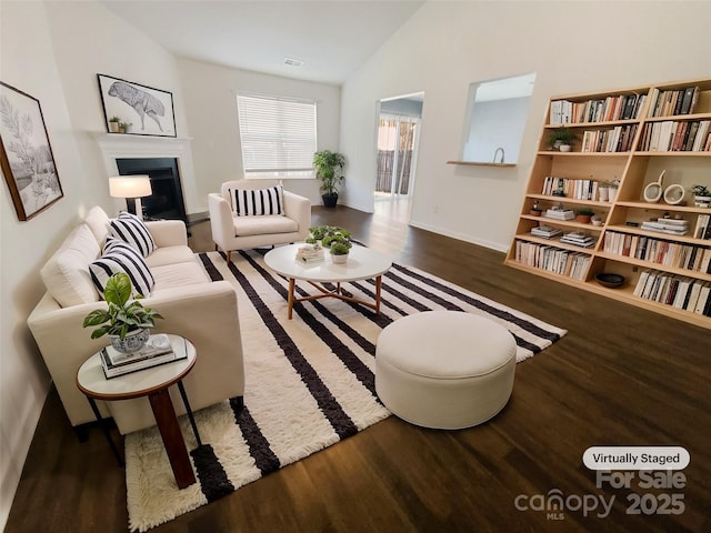 living area featuring visible vents, lofted ceiling, a fireplace with raised hearth, and wood finished floors