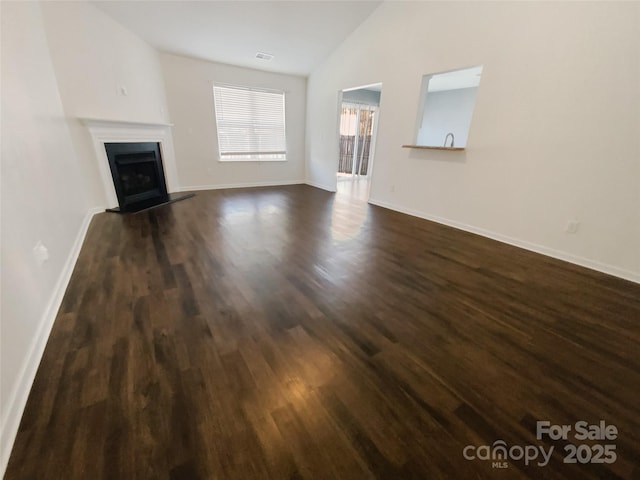 unfurnished living room with visible vents, a fireplace with raised hearth, dark wood finished floors, baseboards, and vaulted ceiling