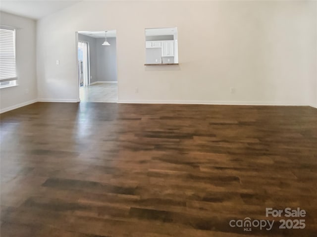 unfurnished room with vaulted ceiling, baseboards, and dark wood-style flooring