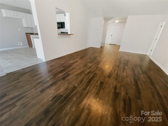 unfurnished living room featuring dark wood-type flooring and baseboards