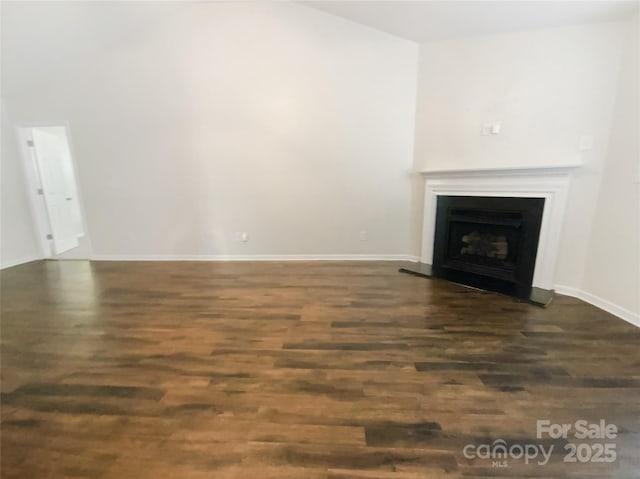 unfurnished living room featuring baseboards, a fireplace with raised hearth, and dark wood finished floors