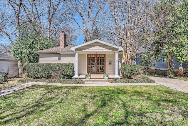 view of front of property with a porch, a chimney, a front lawn, french doors, and brick siding