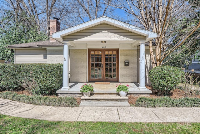 property entrance with french doors, brick siding, covered porch, and a chimney