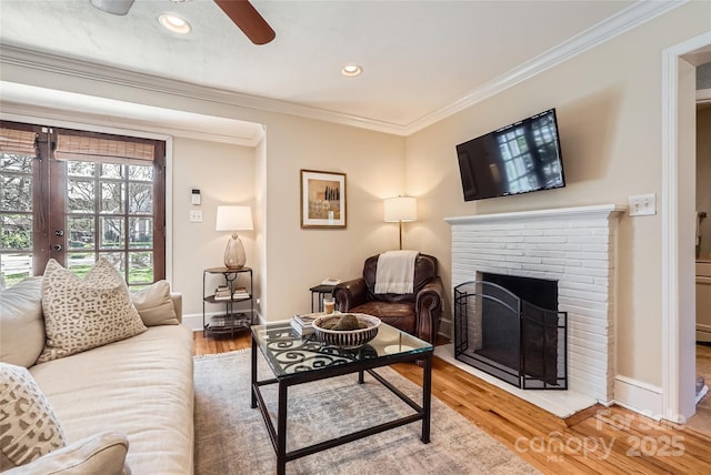 living area with a fireplace, crown molding, light wood-style floors, and baseboards