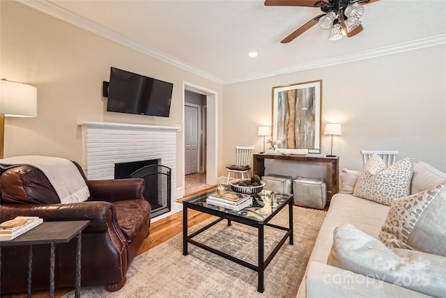 living area featuring light wood finished floors, recessed lighting, a fireplace, ceiling fan, and crown molding