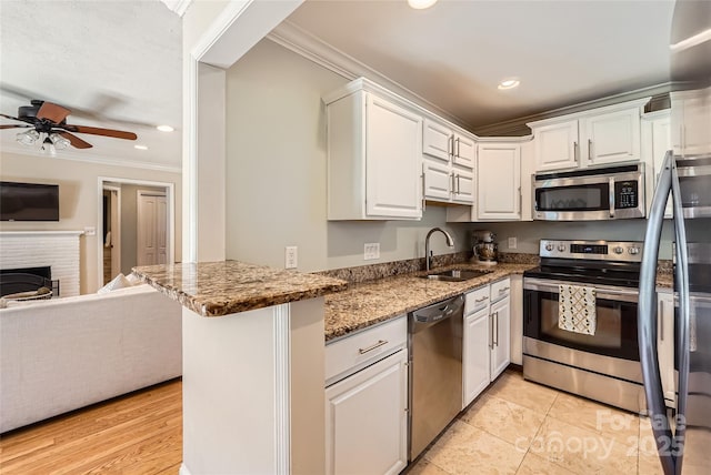 kitchen with a fireplace, a sink, ornamental molding, stainless steel appliances, and white cabinets