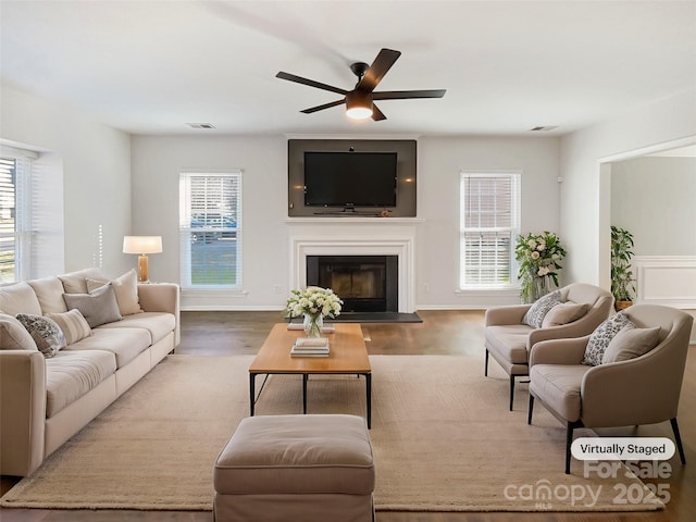 living area featuring a wealth of natural light, wood finished floors, and a glass covered fireplace