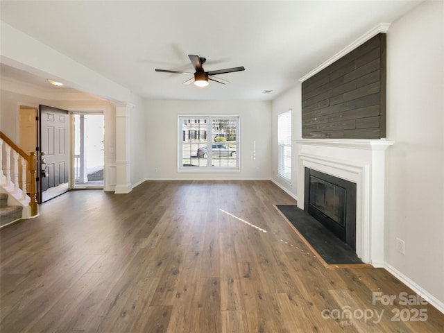 unfurnished living room with ceiling fan, baseboards, stairway, a fireplace with flush hearth, and dark wood-style flooring