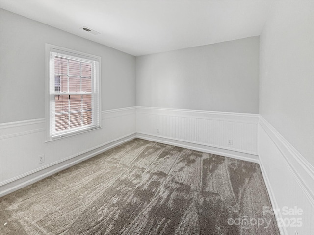 empty room with visible vents, a wainscoted wall, and carpet floors